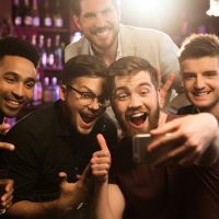 Happy male friends taking selfie and drinking beer at bar or pub